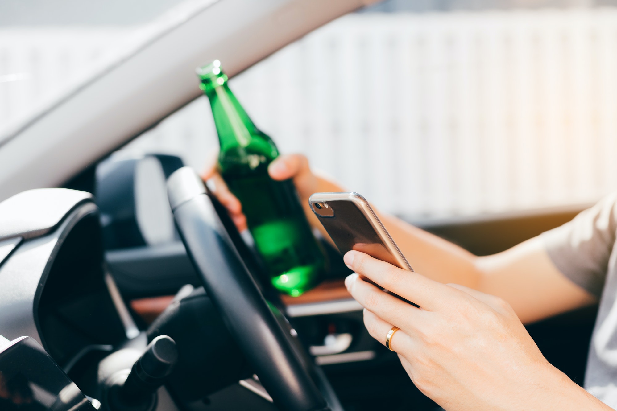 Asian men drink alcohol in the car and using mobile phones while driving.