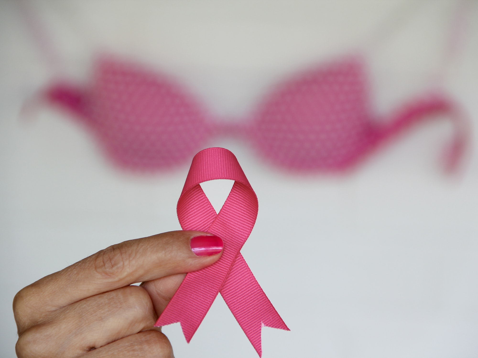 October is Brest Cancer Awareness Month with Woman Holding Pink Ribbon with Pink Bra in Background