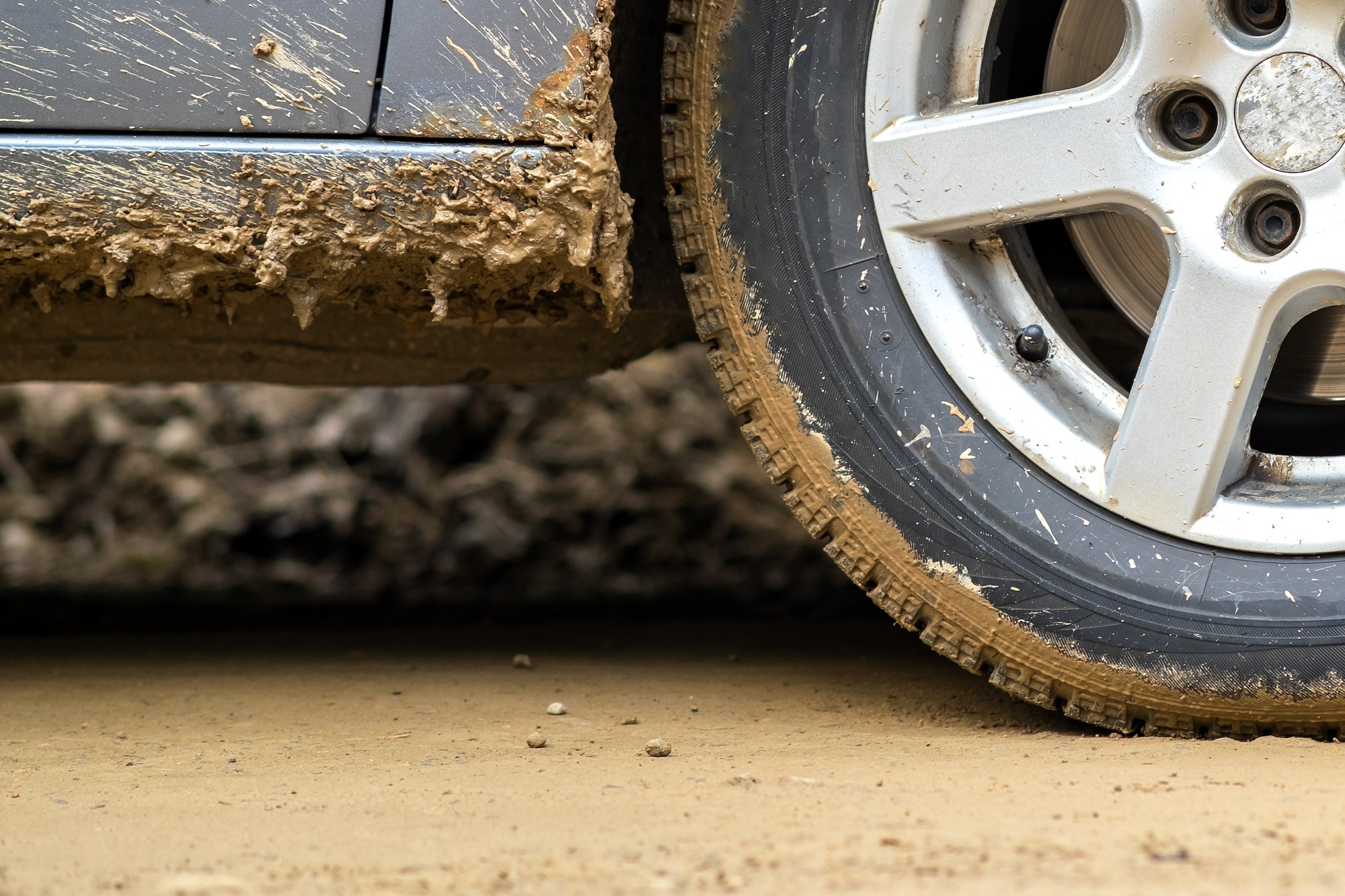 Close up of dirty car wheel with rubber tire covered with yellow mud